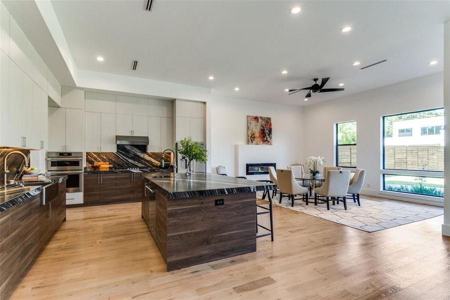 Kitchen with a kitchen bar, light wood-type flooring, ceiling fan, dark stone counters, and a center island with sink