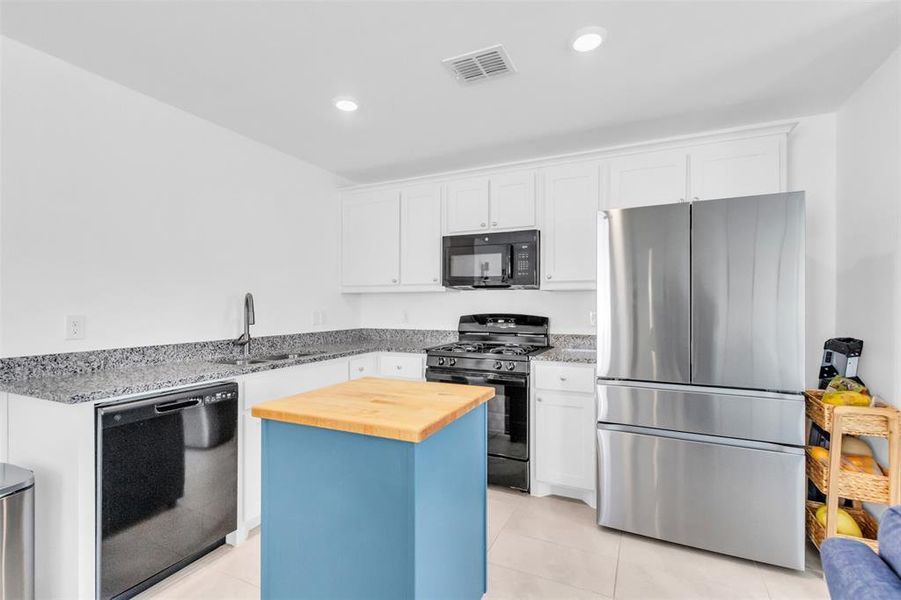 Kitchen with black appliances, butcher block countertops, white cabinetry, light tile patterned floors, and recessed lighting