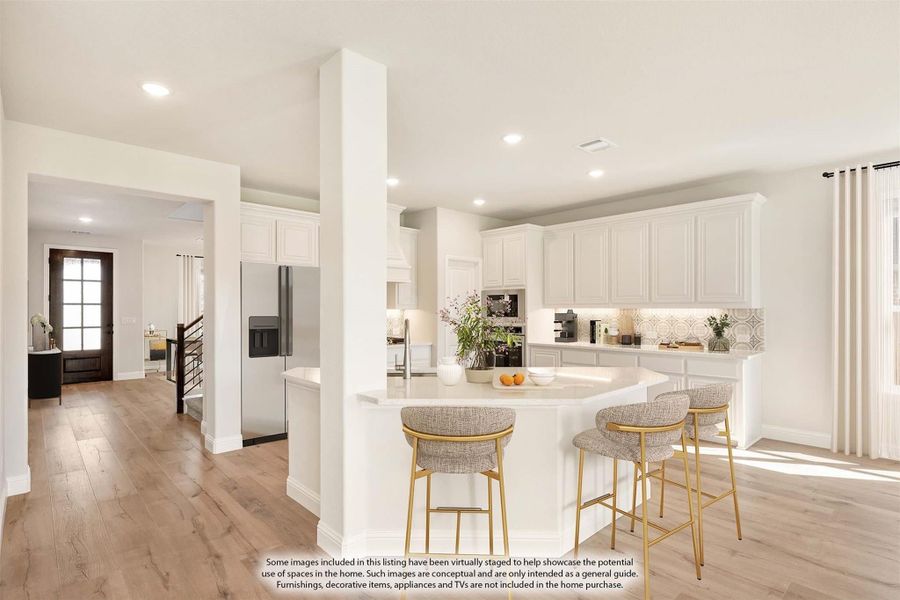 Open kitchen with white cabinets, curved island with bar stools, stainless appliances, and light wood floors