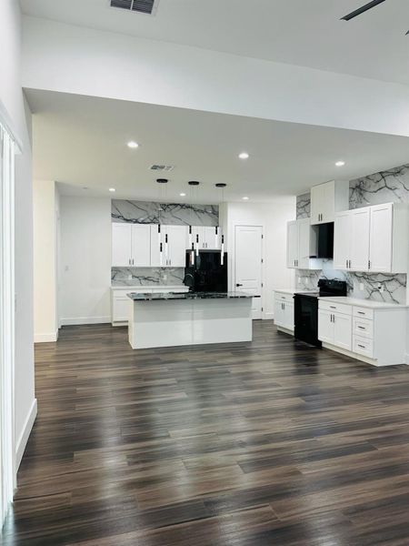 Kitchen featuring backsplash, white cabinetry, black appliances, decorative light fixtures, and an island with sink Kitchen featuring backsplash, white cabinetry, black appliances, decorative light fixtures, and an island with sink
