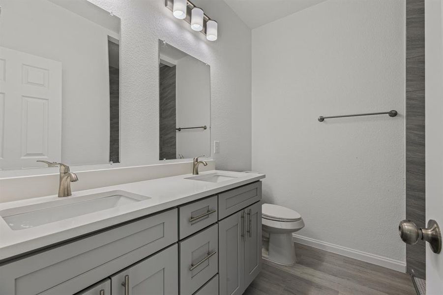 Bathroom with double vanity, light wood-style flooring, and a textured wall