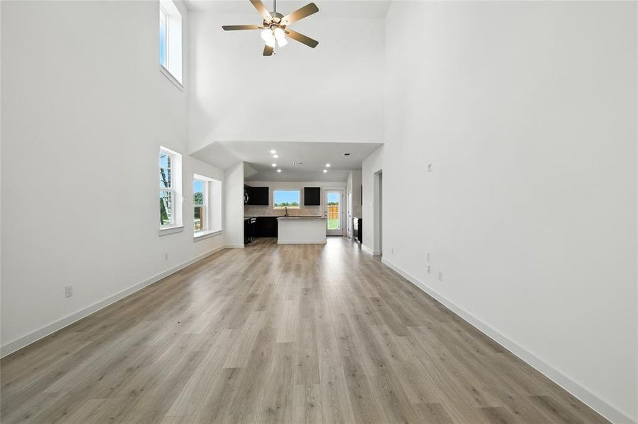 Unfurnished living room featuring a ceiling fan, light wood finished floors, and a high ceiling Unfurnished living room featuring a ceiling fan, light wood finished floors, and a high ceiling
