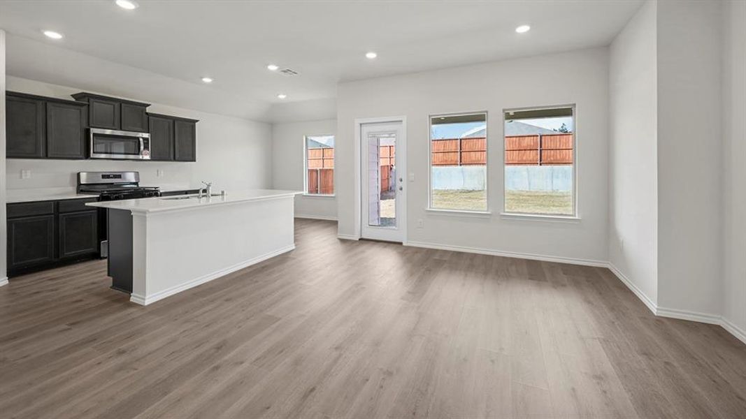 Kitchen with a center island with sink, recessed lighting, appliances with stainless steel finishes, light wood-style flooring, and dark cabinetry