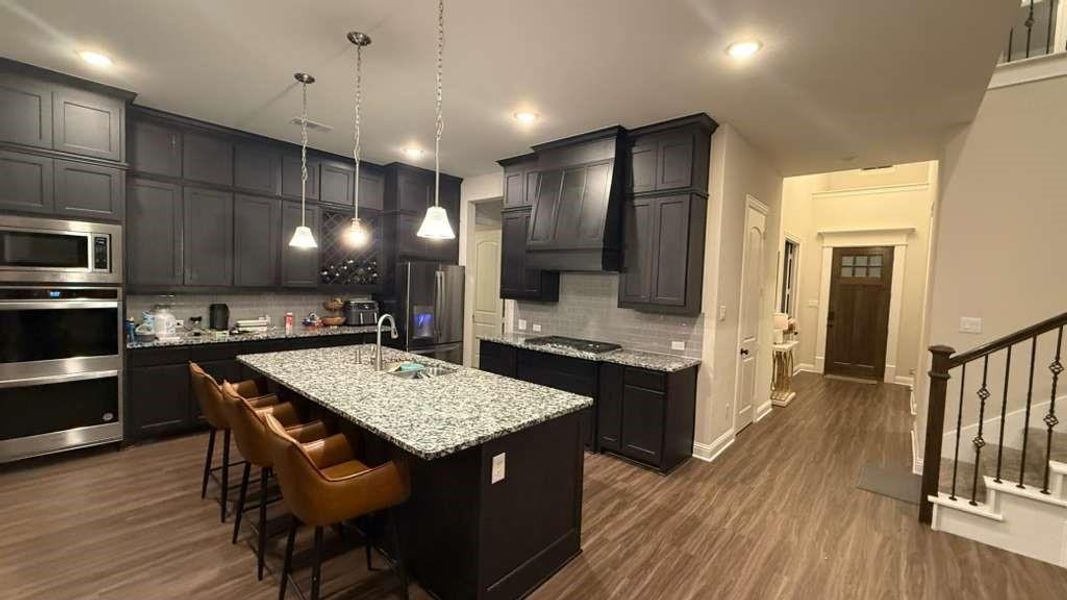 Kitchen featuring appliances with stainless steel finishes, dark wood-style flooring, decorative backsplash, light stone counters, and premium range hood