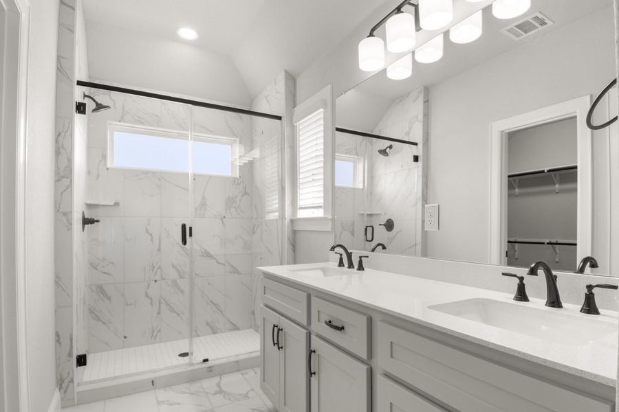 Interior image of a bathroom with dual vanity with grey cabinets and white countertops, and a walk-in shower.