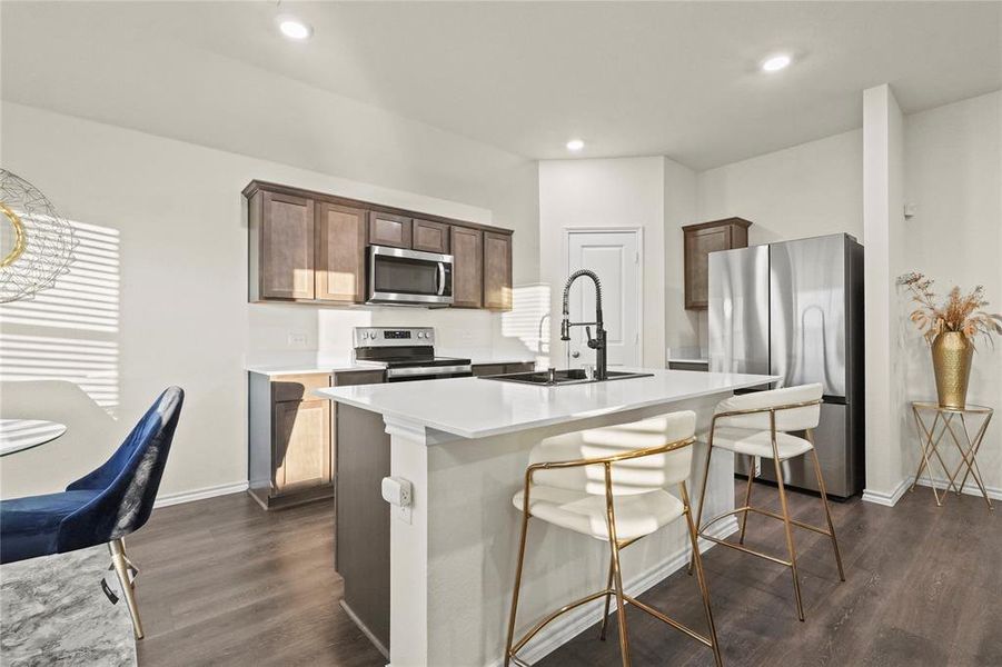 Kitchen featuring wood-style floors, a kitchen island with sink, sink, appliances with stainless steel finishes, and dark brown cabinetry