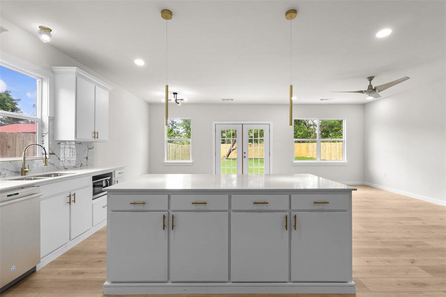 Spacious kitchen and living area featuring a central island with countertop, recessed lighting, wood-finish flooring, white cabinetry with gold-tone hardware, and a ceiling fan