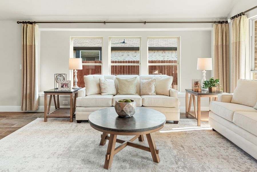 Living room with cream sofa, round wood coffee table, and large windows with neutral curtains