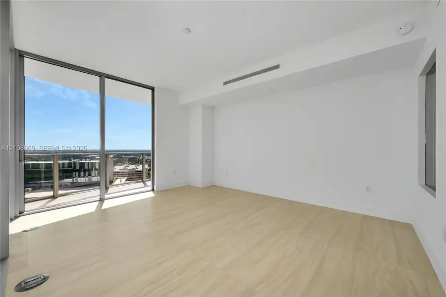 Floor-to-ceiling glass sliding doors, private balcony, wood-finish flooring, and minimalist white interior walls