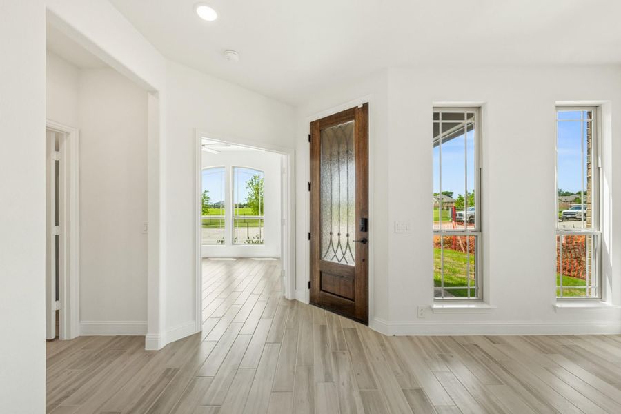 Bright home entryway with dark wood front door, glass panels, and light wood-look tile floors Bright home entryway with dark wood front door, glass panels, and light wood-look tile floors