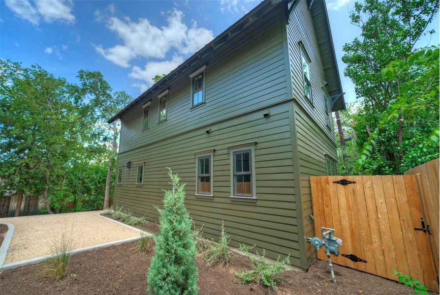 A striking green exterior with wood fencing offers a modern aesthetic amidst lush landscaping and a gravel drive.