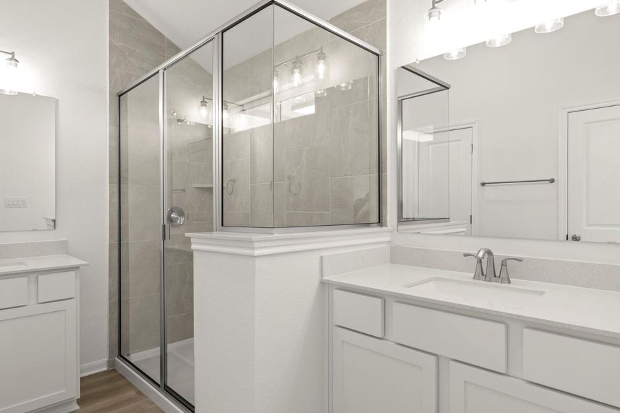 Full bath featuring two vanities, a shower stall, and wood finished floors