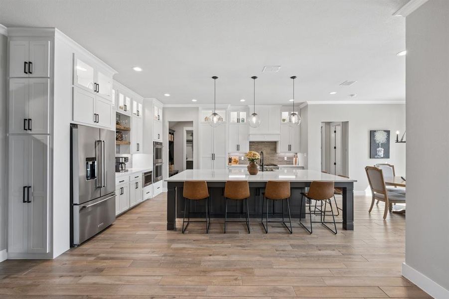 Two tone kitchen featuring glass insert cabinets, crown molding, stainless steel appliances, a large island with sink, and two tone cabinets