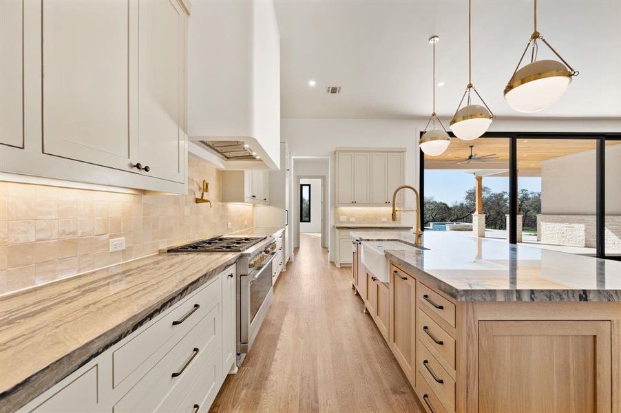 Kitchen with light stone countertops, high end range, light wood finished floors, a large island, and pendant lighting