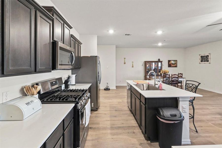 Kitchen featuring stainless steel appliances, light wood-style flooring, a breakfast bar, an island with sink, and recessed lighting