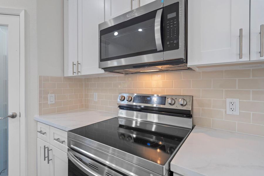 This photo highlights the modern kitchen appliances, featuring a sleek stainless steel electric range and built-in microwave. The glossy subway tile backsplash and white quartz countertops create a clean, contemporary look.