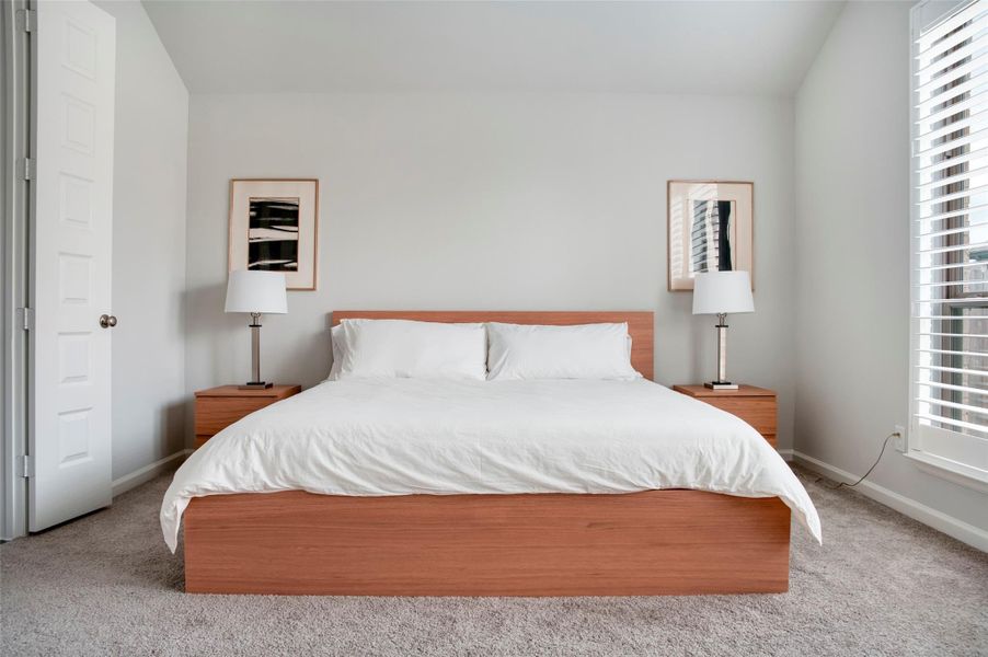 This bedroom features a modern, minimalist design with a comfortable bed, wooden side tables, and matching lamps. The room is bright with neutral walls and carpet, enhanced by natural light from large windows with blinds. This bedroom features a modern, minimalist design with a comfortable bed, wooden side tables, and matching lamps. The room is bright with neutral walls and carpet, enhanced by natural light from large windows with blinds.