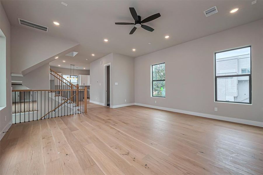 Discover this modern, open-concept living area featuring light wood flooring, a sleek fireplace, and a ceiling fan. The elegant staircase with wooden steps and a black iron railing leads to the upper level, while expansive windows and glass doors flood the space with natural light.