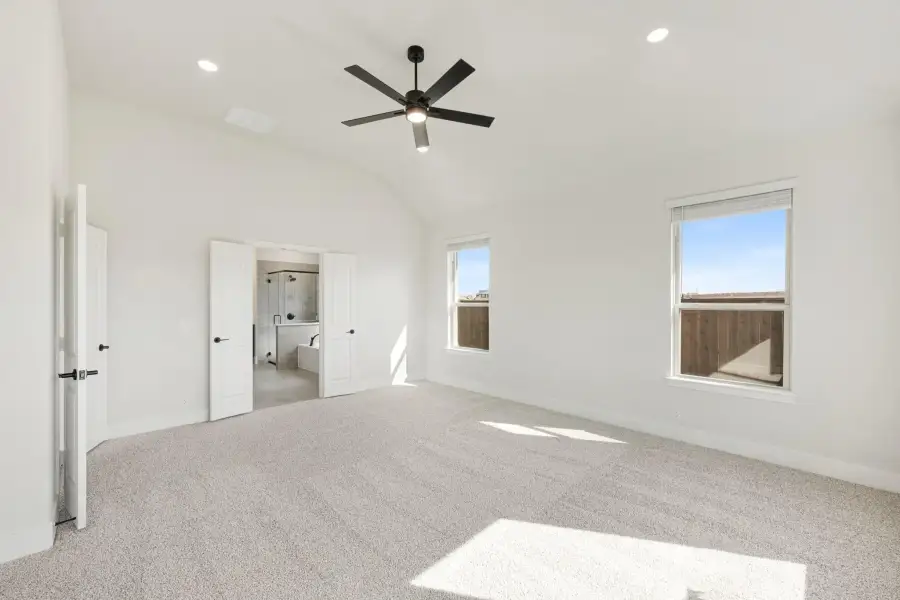 Spacious master bedroom with vaulted ceiling, ceiling fan, carpet floors, and ensuite bathroom access