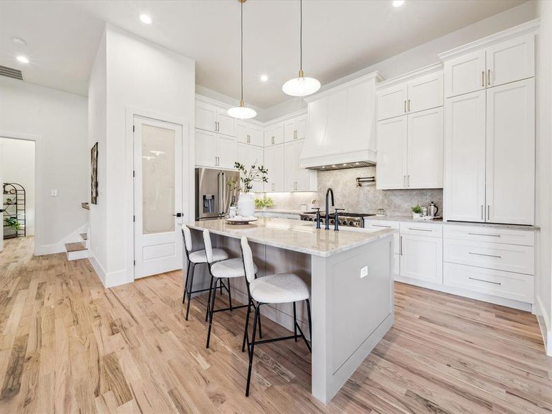 Kitchen with white cabinetry, light hardwood / wood-style flooring, premium range hood, an island with sink, and high quality fridge