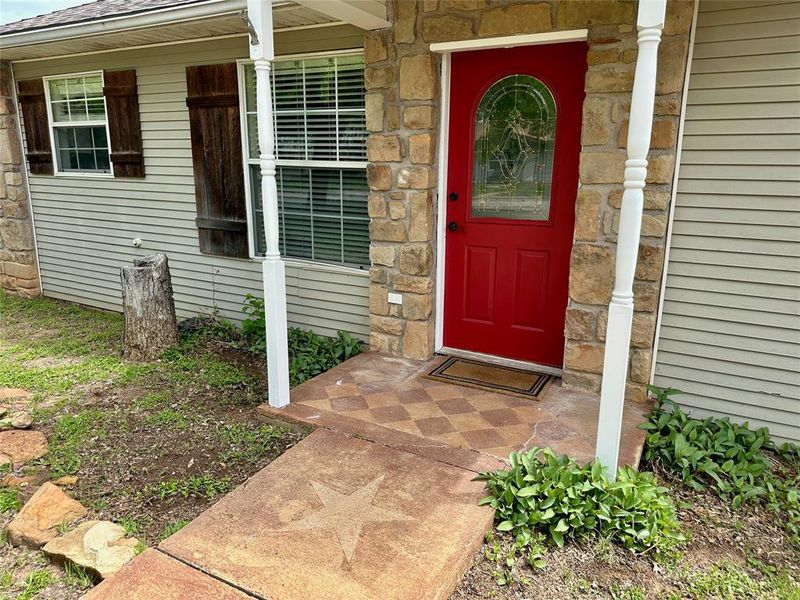 Property entrance featuring stone siding, covered porch, and roof with shingles