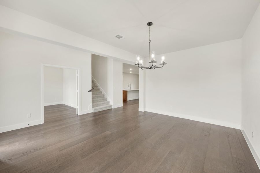 Open living and dining area with dark hardwood floors, chandelier, and staircase visible in background.