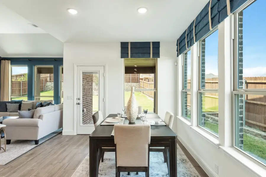 Dining area with dark wood table, cream chairs, large windows, and open view to living room and backyard
