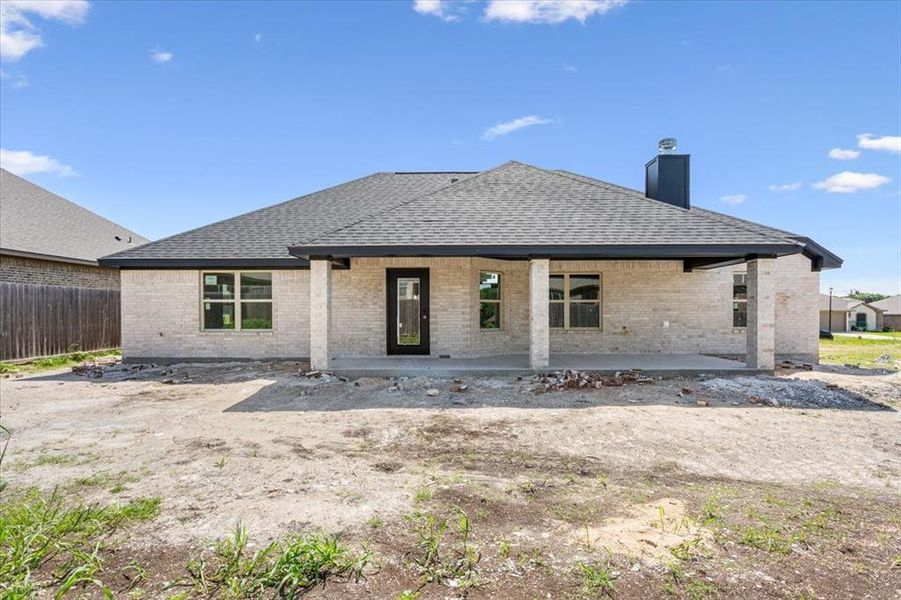 Rear view of property featuring a shingled roof, brick siding, a chimney, and a patio area Rear view of property featuring a shingled roof, brick siding, a chimney, and a patio area