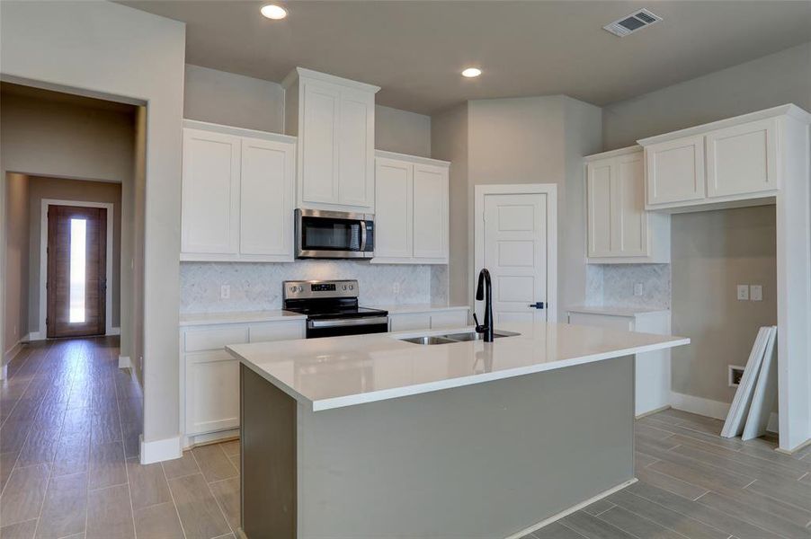 Kitchen featuring stainless steel appliances, sink, a center island with sink, and white cabinets