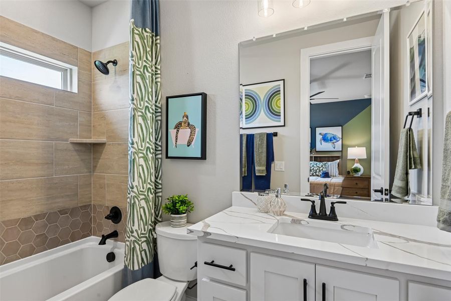Bathroom with white vanity, quartz countertop, and tub-shower combo with tan tile surround and patterned curtain Bathroom with white vanity, quartz countertop, and tub-shower combo with tan tile surround and patterned curtain