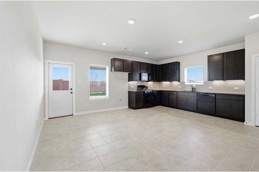 Spacious kitchen featuring dark wood cabinetry, solid surface countertops, a full suite of black appliances, and recessed lighting Spacious kitchen featuring dark wood cabinetry, solid surface countertops, a full suite of black appliances, and recessed lighting