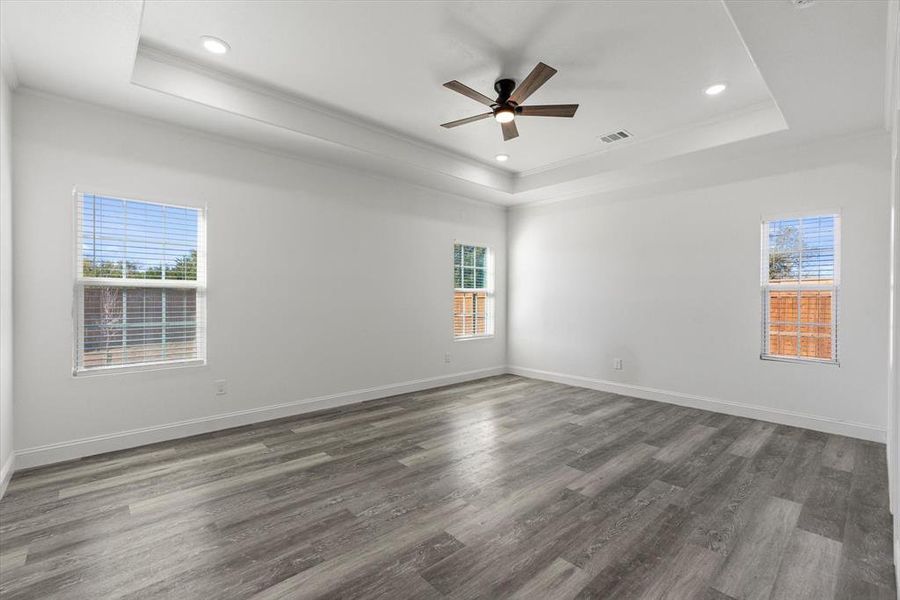 Empty room with a raised ceiling, ceiling fan, dark wood-type flooring, and ornamental molding
