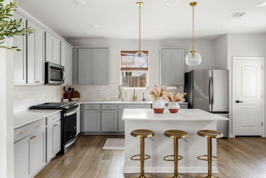 Kitchen with stainless steel appliances, a kitchen bar, light wood-style floors, a center island, and hanging light fixtures