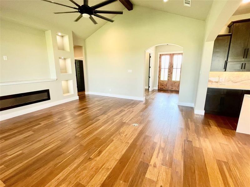 Unfurnished living room featuring light hardwood / wood-style floors, french doors, beamed ceiling, high vaulted ceiling, and ceiling fan