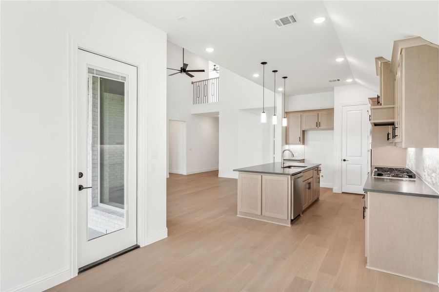 Open kitchen with center island, light wood cabinets, pendant lights, and hardwood floors open to living area