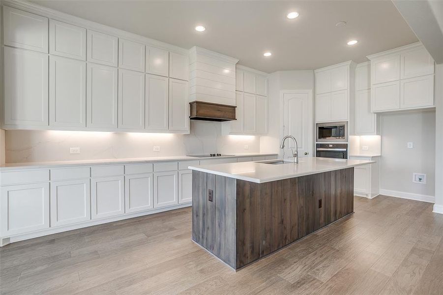 Kitchen with white cabinets, a center island with sink, light wood-type flooring, custom range hood, and stainless steel appliances