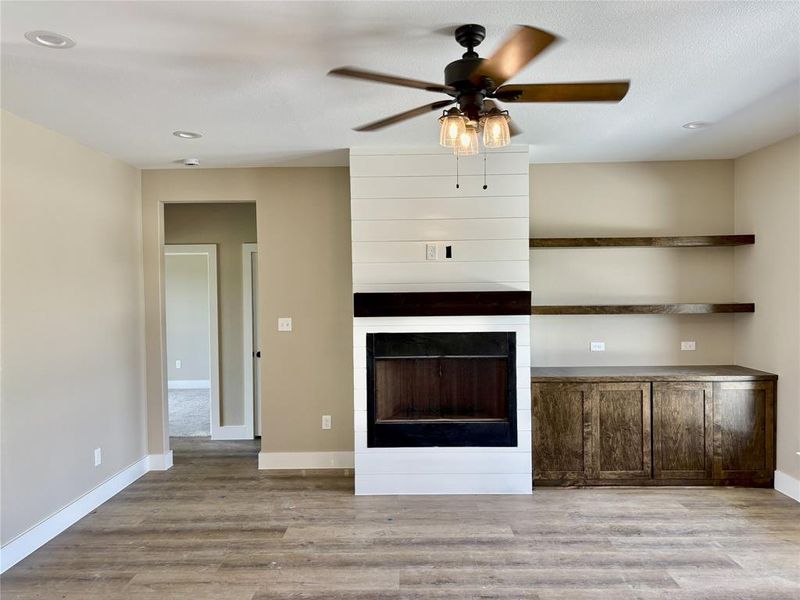 Unfurnished living room with wood finished floors, a ceiling fan, a tiled fireplace, and recessed lighting Unfurnished living room with wood finished floors, a ceiling fan, a tiled fireplace, and recessed lighting