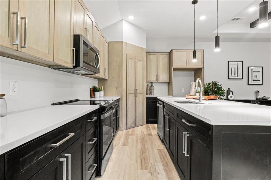 Kitchen featuring sink, stainless steel appliances, light hardwood / wood-style flooring, pendant lighting, and a center island with sink