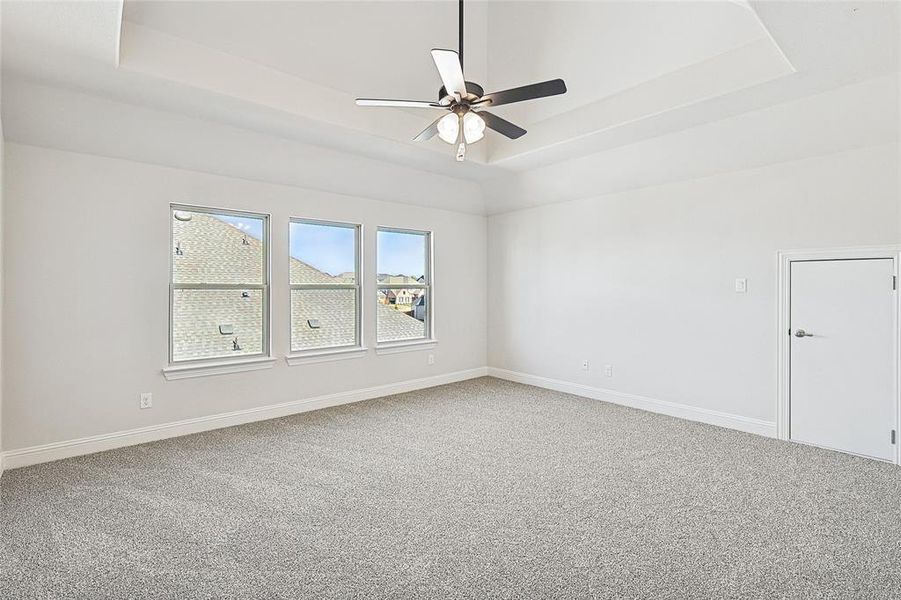 Carpeted empty room with a raised ceiling and ceiling fan