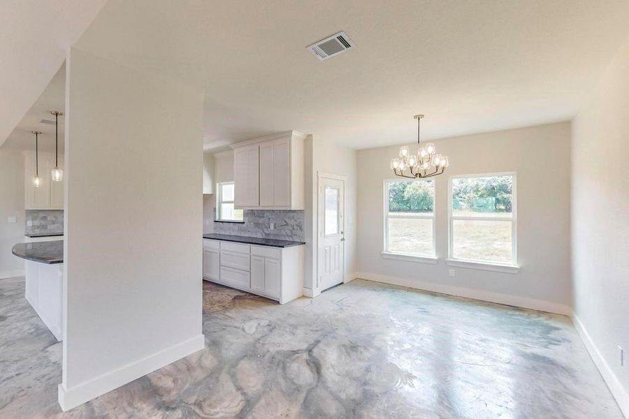 Kitchen with tasteful backsplash, hanging light fixtures, a notable chandelier, and white cabinetry