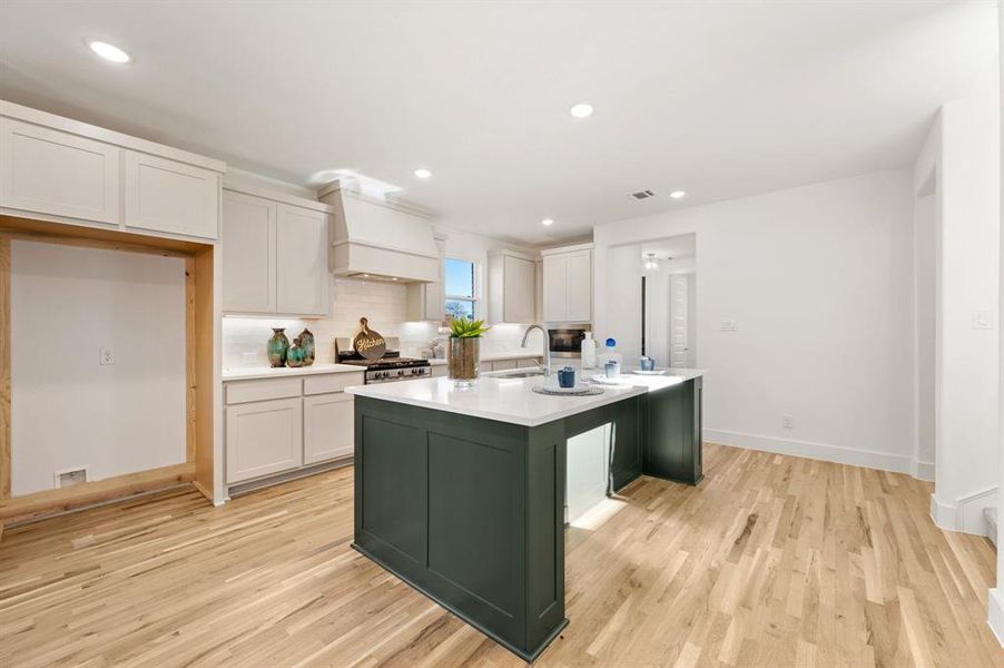 Kitchen with decorative backsplash, an island with sink, two tone color scheme, light wood-type flooring, and recessed lighting