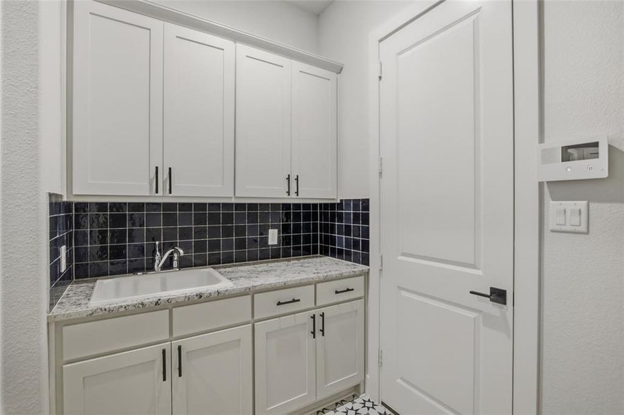 Kitchen with white cabinetry, light stone countertops, a textured wall, and decorative backsplash
