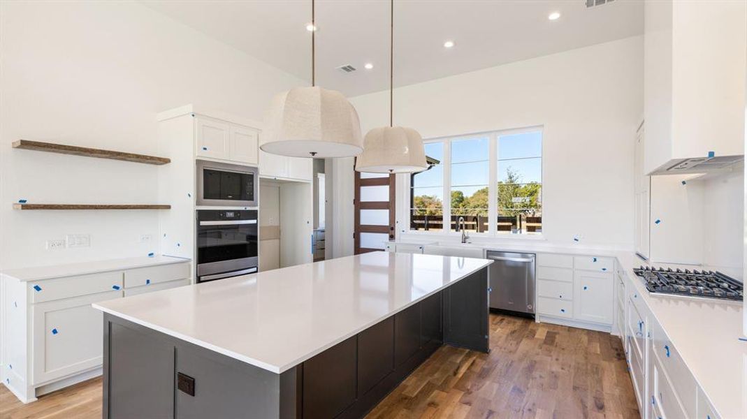 Kitchen with dark wood-type flooring, white cabinets, stainless steel appliances, and decorative light fixtures