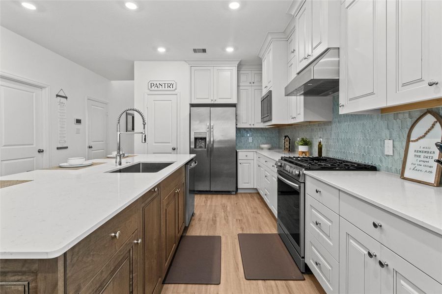 Sleek kitchen featuring a spacious island with a modern sink, stainless steel appliances, and ample cabinet space. The elegant backsplash and wood flooring add a warm touch to this inviting culinary space. Sleek kitchen featuring a spacious island with a modern sink, stainless steel appliances, and ample cabinet space. The elegant backsplash and wood flooring add a warm touch to this inviting culinary space.
