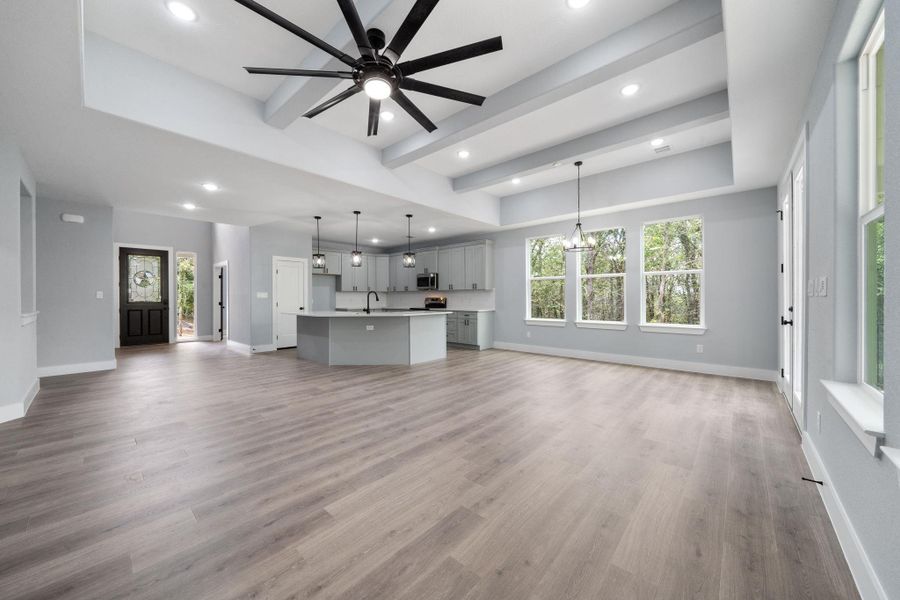 Expansive open-concept living area featuring wood-finish flooring and a vaulted ceiling with exposed beams