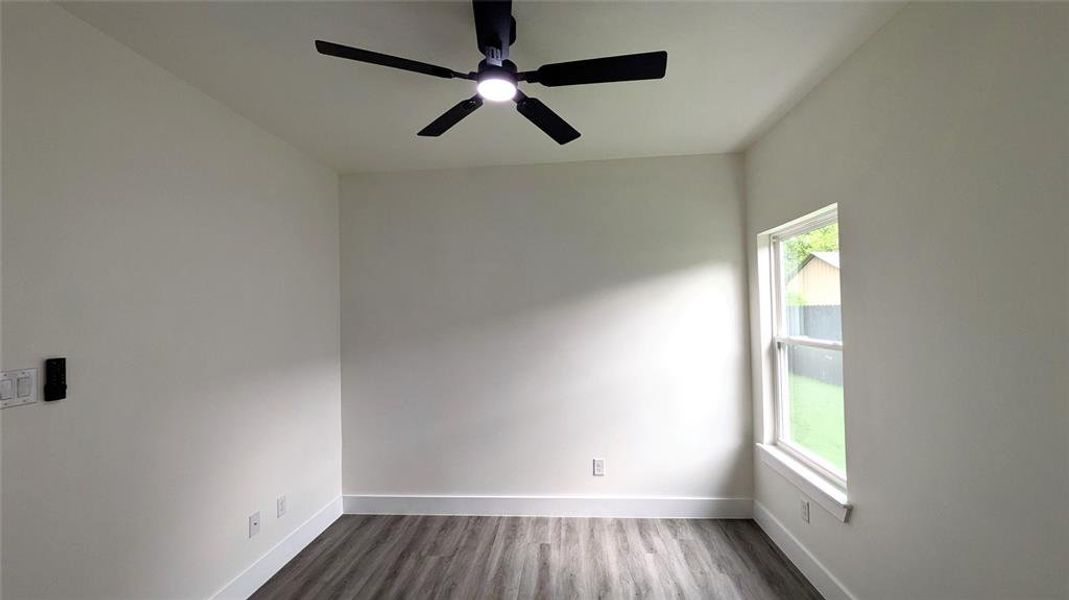 Spare room featuring dark wood-type flooring, a ceiling fan, baseboards, and a wealth of natural light
