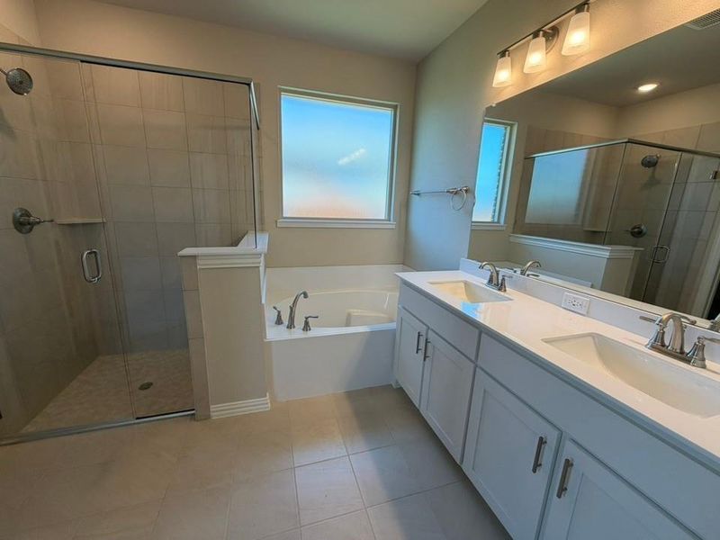 Bathroom featuring a dual vanity with white cabinetry and undermount sinks, a large soaking tub, and a glass-enclosed shower