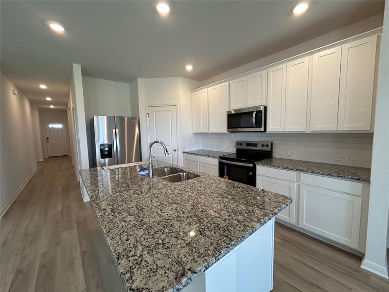 Kitchen with backsplash, appliances with stainless steel finishes, white cabinetry, light wood-type flooring, and dark stone counters Kitchen with backsplash, appliances with stainless steel finishes, white cabinetry, light wood-type flooring, and dark stone counters