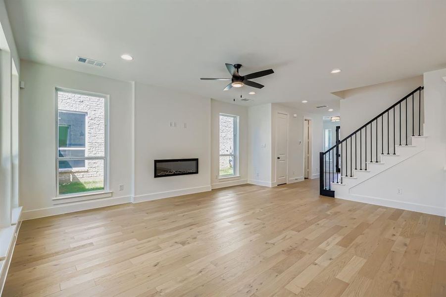 Unfurnished living room with a glass covered fireplace, stairs, light wood-style floors, recessed lighting, and ceiling fan