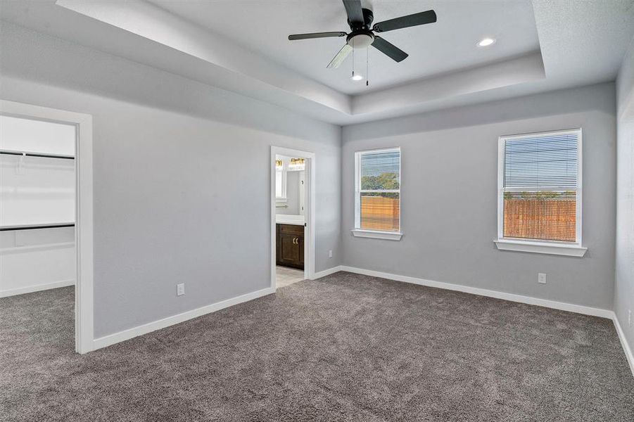 Unfurnished bedroom with a spacious closet, ceiling fan, a raised ceiling, ensuite bathroom, and a closet